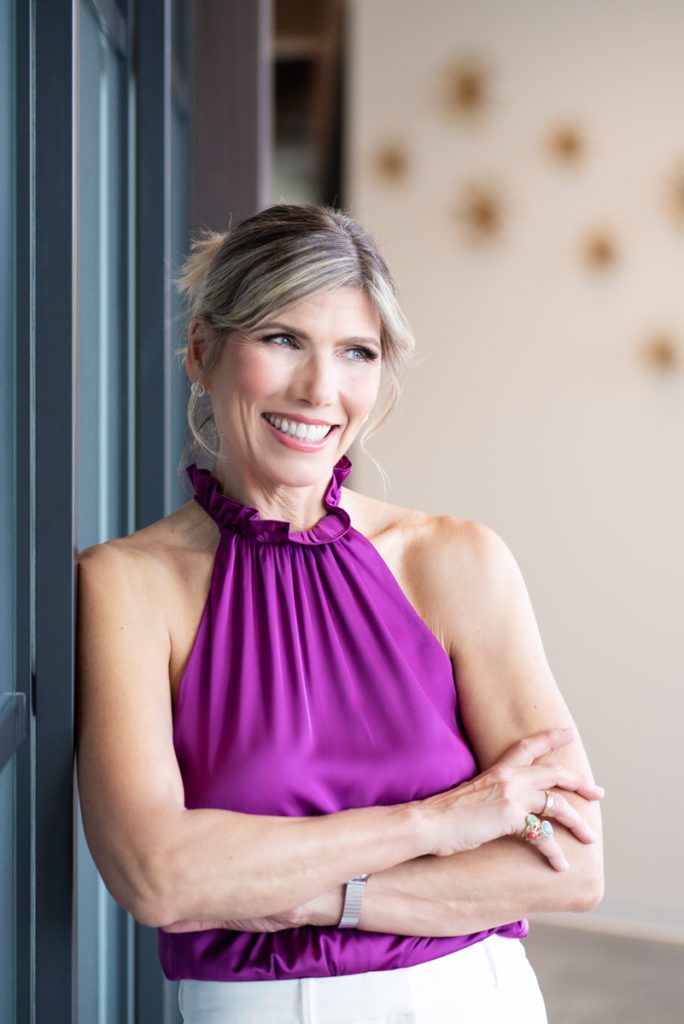 Woman leans against a wall smiling during her personal branding photo shoot. 