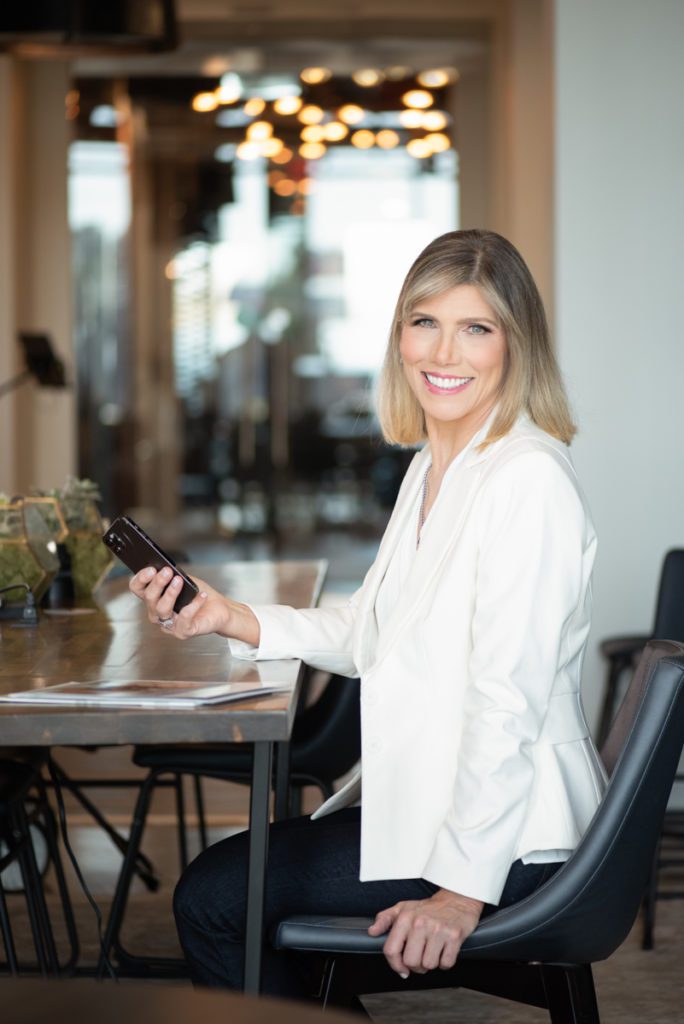Woman sits at a desking smiling while holding her phone. 