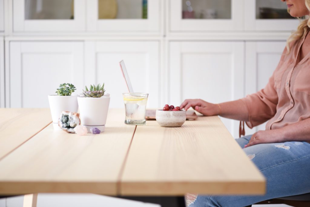 A woman's hand touches a computer at a table with plants and food.