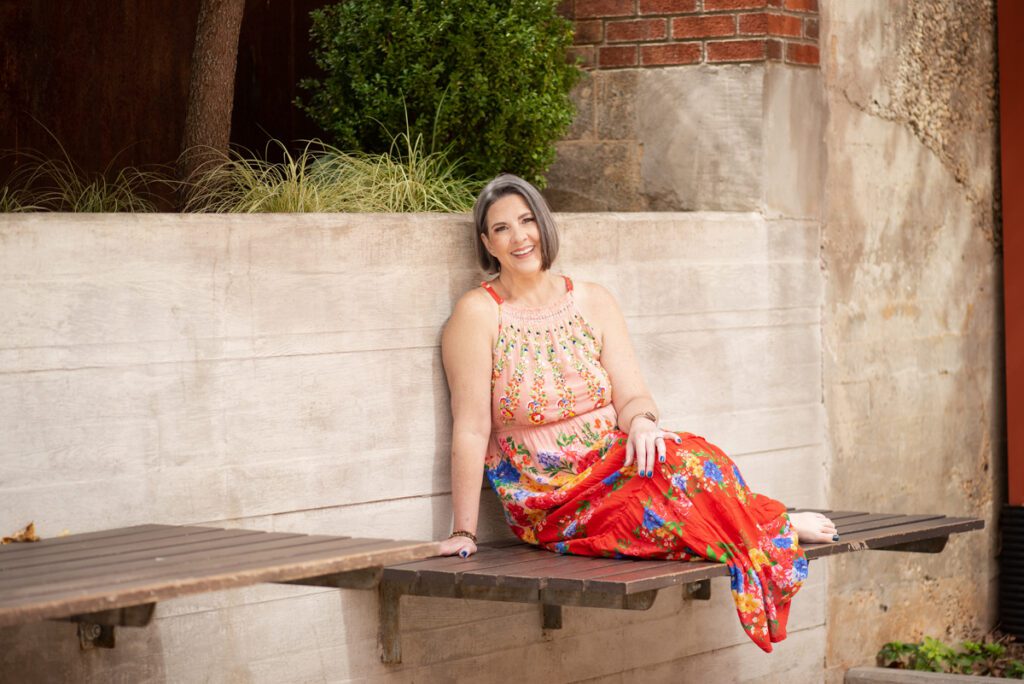 A woman lounges on a wooden bench, smiling with her feet up. 